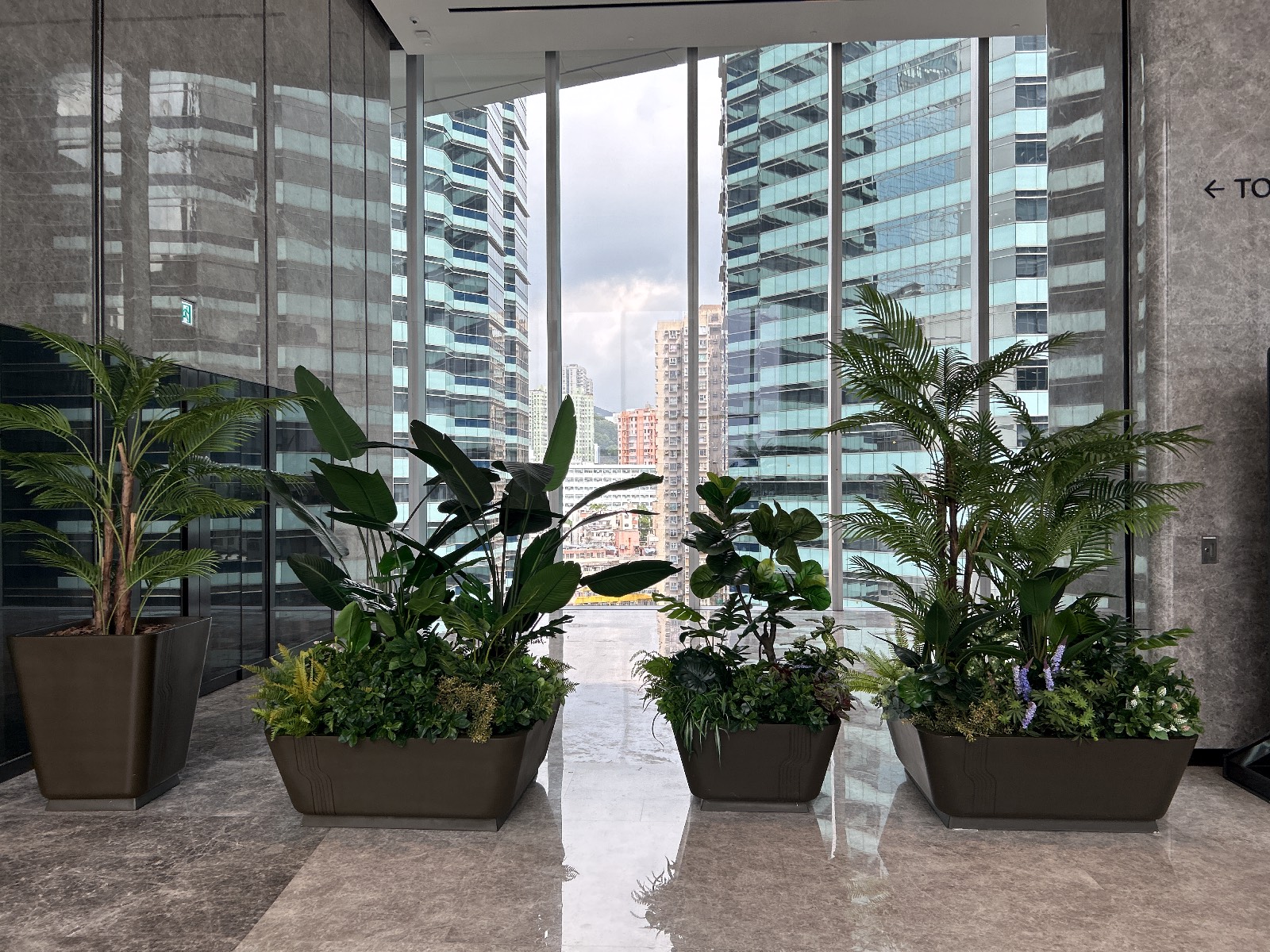 The Millennity Lobby Planters · Hong Kong · BEE Incorporations The Millennity lobby with large biophilic planters framing a Hong Kong skyline view, a WELL Platinum office interior